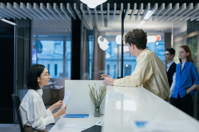 Employees interacting at a sleek office reception desk, fostering professional collaboration. Coordinating joiner and leaver requests