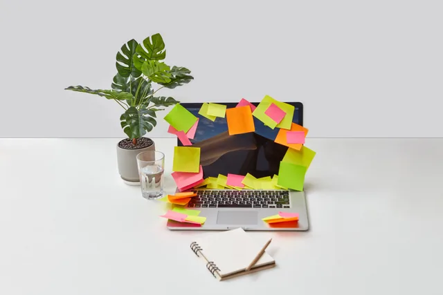 Laptop covered with colorful sticky notes on a modern desk with plant and notebook. Process automation versus task shortcuts